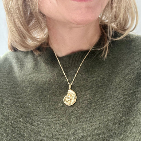women in a green sweater wearing a gold ammonite pendant necklace