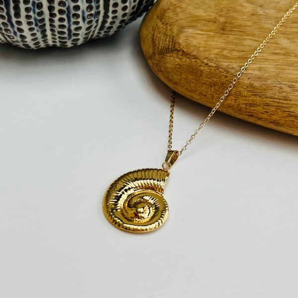 gold ammonite pendant lying on a wooden heart on a white table