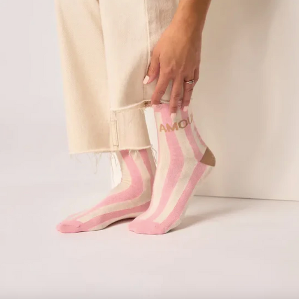 Person wearing pink and white striped socks with 'AMORE' text on a plain background