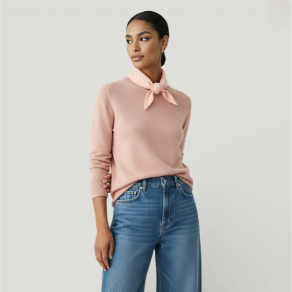 Woman wearing a pink sweater with a pale pink tied scarf and blue jeans on a light grey background