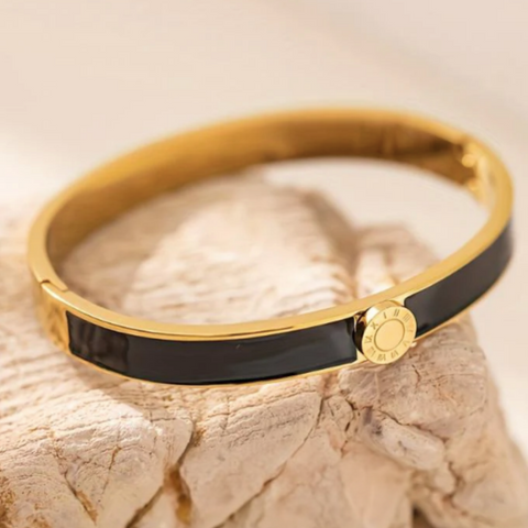 Gold and black enamel bracelet on a textured surface