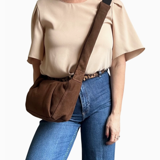 woman in cream top and blue jeans wearing a brown suede crossbody bag