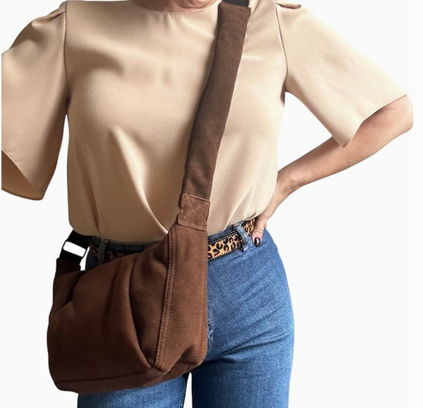 Person wearing a beige blouse, blue jeans, and carrying a brown suede shoulder bag on a white background