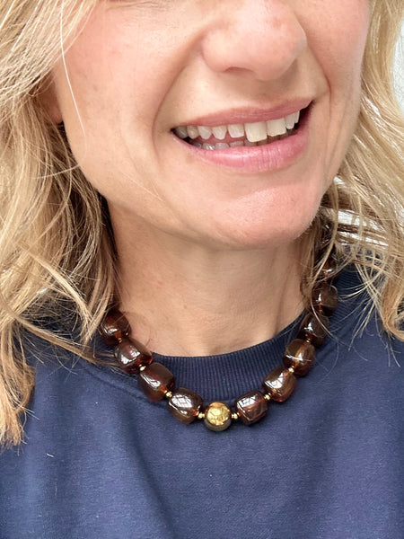 Close-up of a person wearing a brown beaded necklace with a blue shirt.