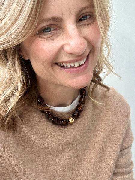 Woman wearing a beige sweater and a brown and gold beaded necklace with a white background