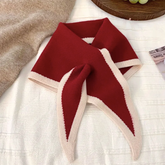 Red and beige skinny knit scarf on a white surface with a blurred background