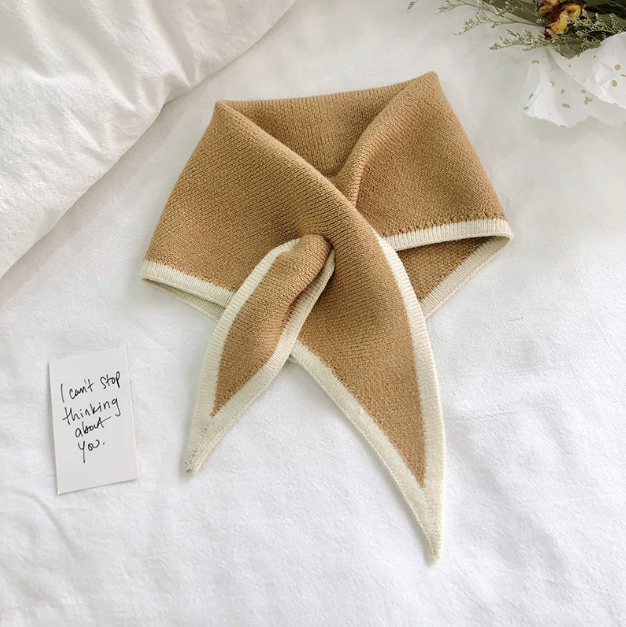 Brown and beige folded scarf on a white surface with a small card.