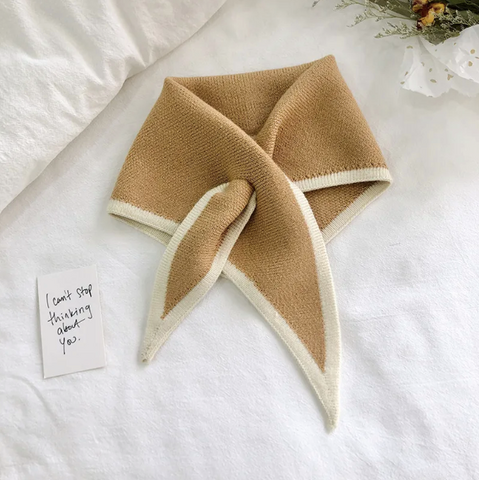 Brown and beige folded scarf on a white surface with a small card.
