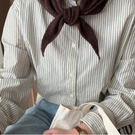 Woman wearing a striped shirt with a chocolate brown skinny triangle scarf tied around the neck, holding a beige bag.
