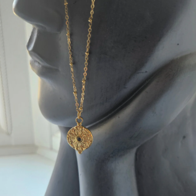Gold and black necklace with a decorative pendant on a mannequin head.