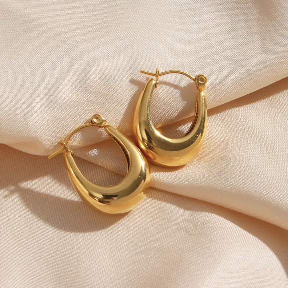 A pair of polished gold crescent hoop earrings with a teardrop shape, displayed on a textured beige fabric background.