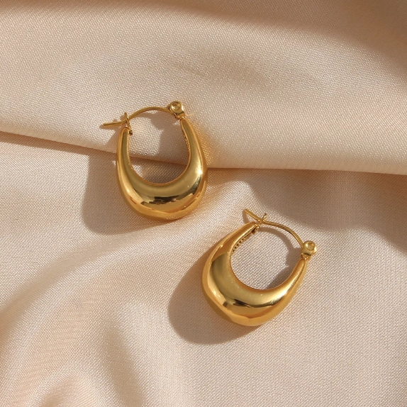 A pair of polished gold crescent-shaped hoop earrings resting on draped beige satin fabric.