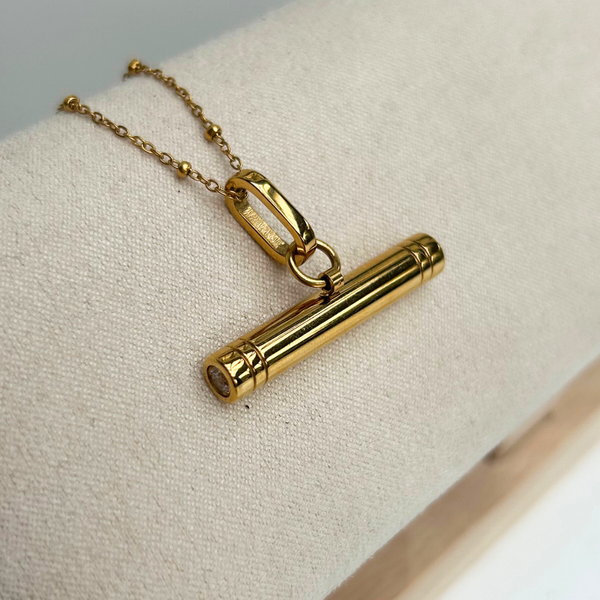 gold T-Bar pendant on a satellite chain on a cream linen jewellery hanger