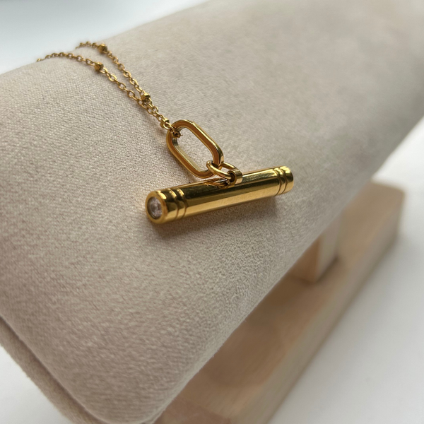 gold T-Bar pendant on a satellite chain on a cream linen jewellery hanger