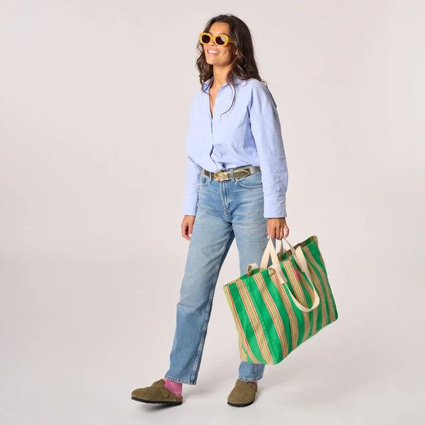Woman holding a green and pink striped bag against a plain background