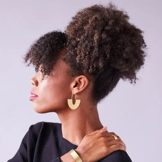 Woman with styled hair wearing gold earrings and bracelets against a plain background