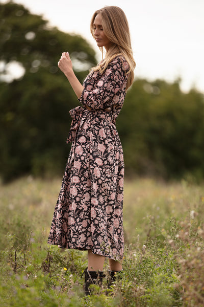 Woman in a floral dress standing in a field with blurred greenery in the background