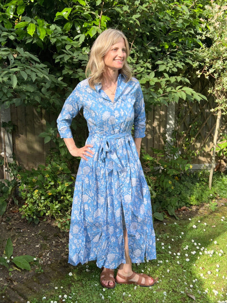 Woman in a blue floral shirt dress standing in a garden