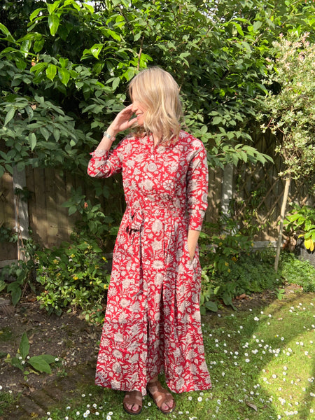 Woman wearing a red floral dress standing in a garden.