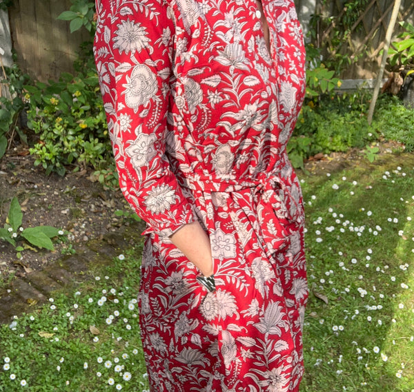 Person wearing a red floral dress standing in a garden with hands in pockets