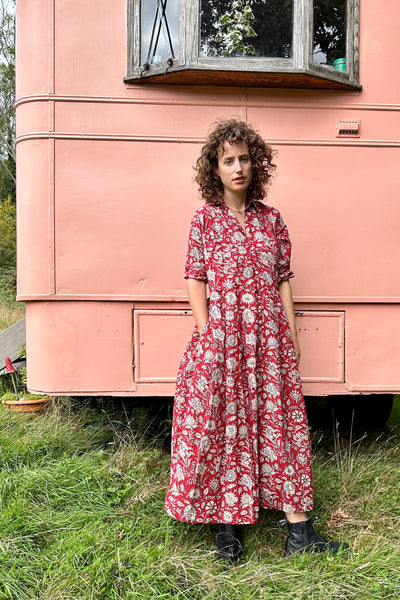 Woman in a red floral dress standing in front of a pink trailer.