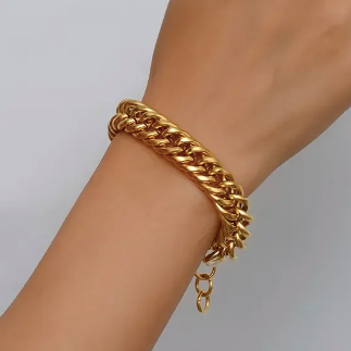 A gold-toned double-strand Cuban link chain bracelet worn on a person's wrist, shown against a plain light gray background.