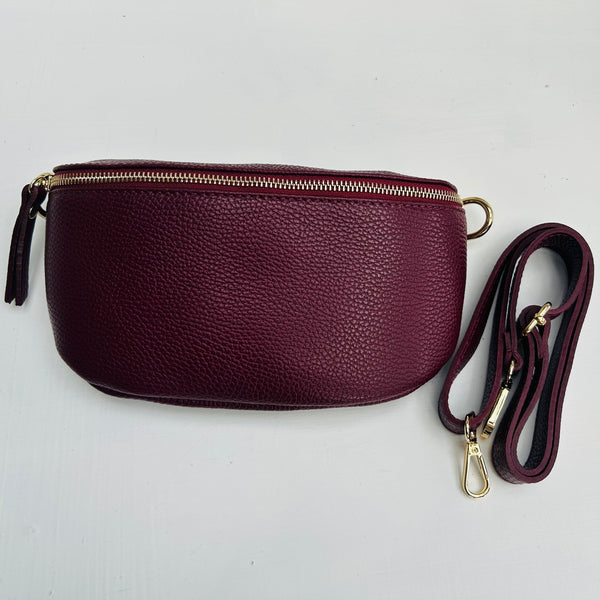 Burgundy leather crossbody bag with a strap on a light gray background
