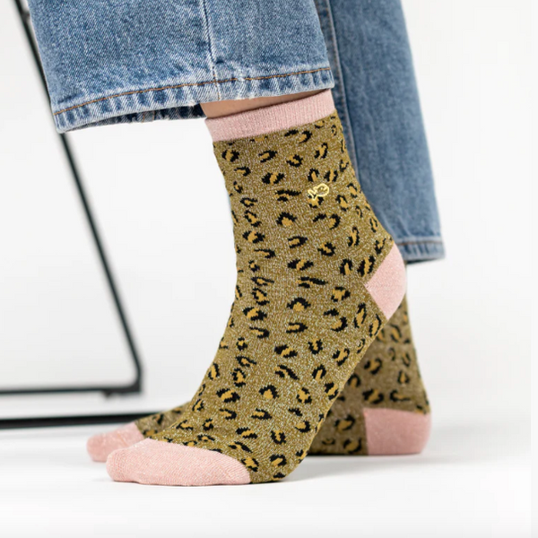 Person wearing jeans with green and pink leopard print socks with a white background