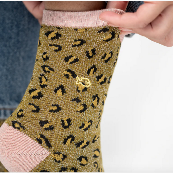 Green sock with black leopard print  aand pink cuffs worn by a person against a white background