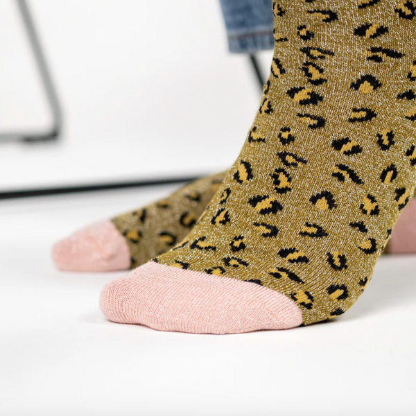 Leopard print olive green ocks with pink toes worn by a person on a white background