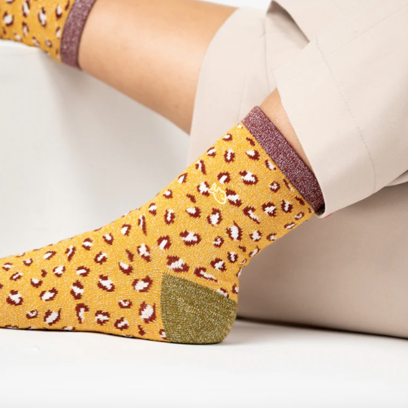 Yellow socks with a leopard print pattern worn by a person sitting on a white surface.