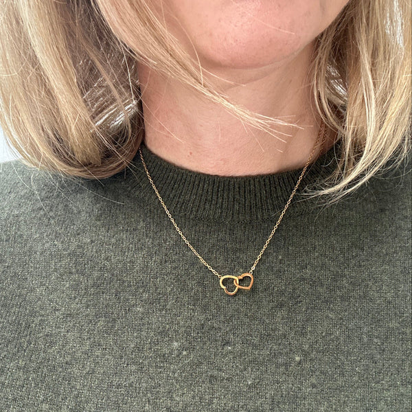woman in a green sweater wearing a gold interlinked hearts necklace