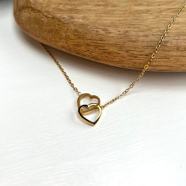 Two hearts interlocked pendant on a gold chain.  Lying on a wooden heart on a white background