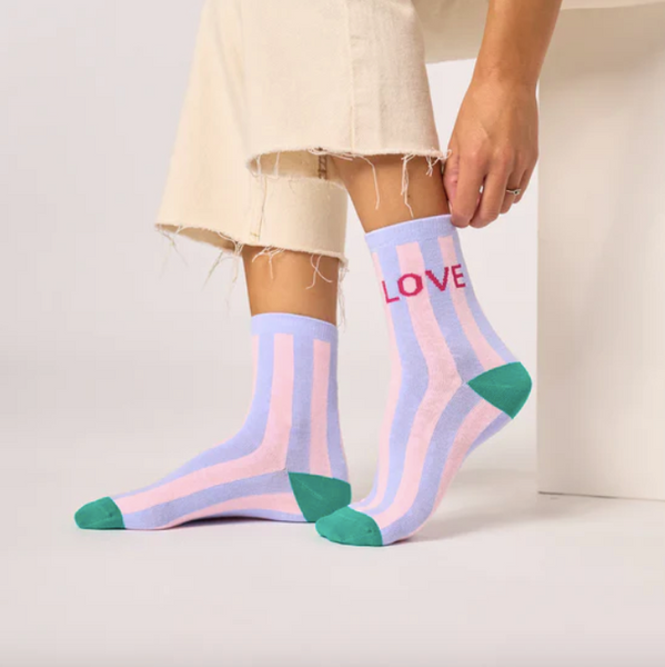 Person wearing colorful striped socks with 'LOVE' on a neutral background