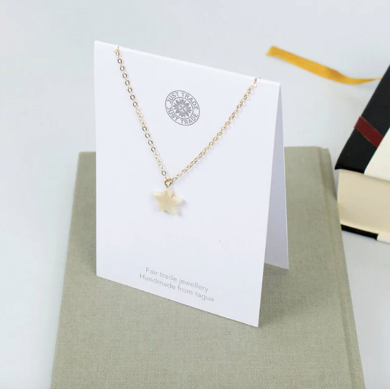 Gold necklace with a star pendant on a white card with branding, placed on a textured surface.