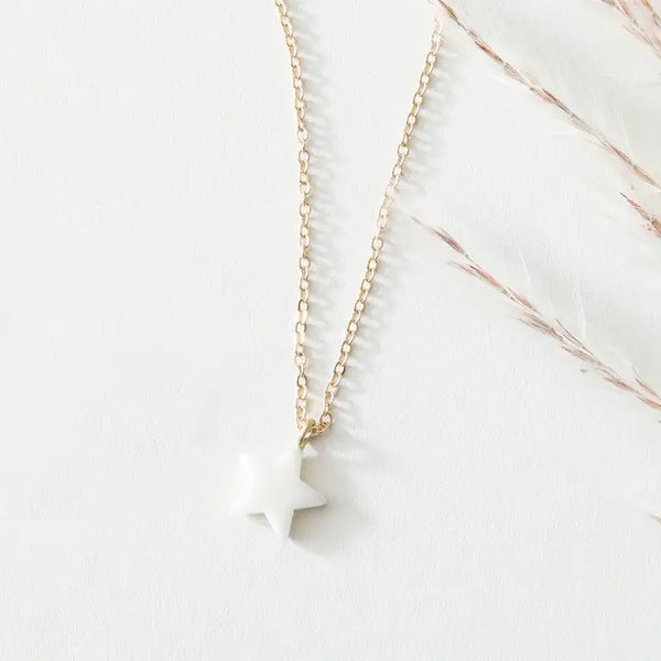 Gold necklace with a white pendant on a light pink background