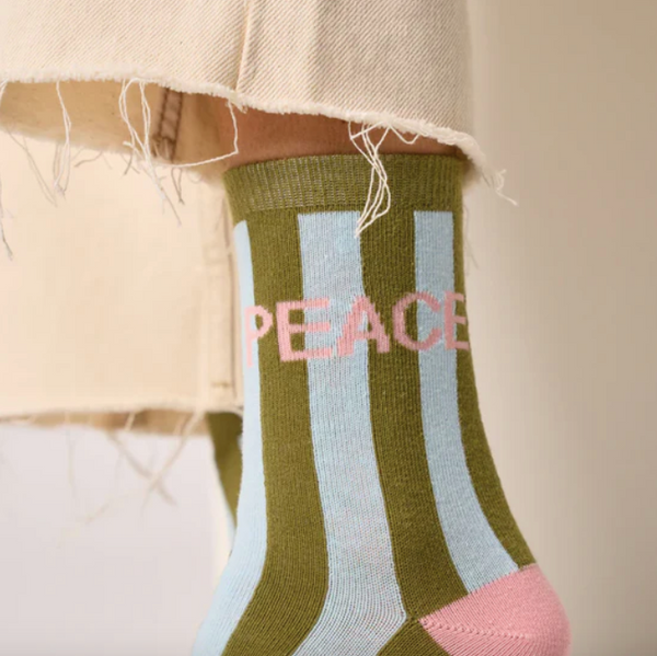 Striped socks with 'PEACE' text worn by a person wearing cream jeans with a blurred background.
