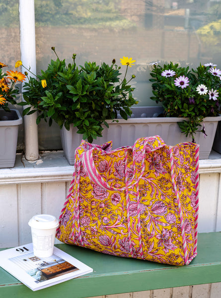 Floral-patterned yellow and pink bag on a table with potted plants in the background