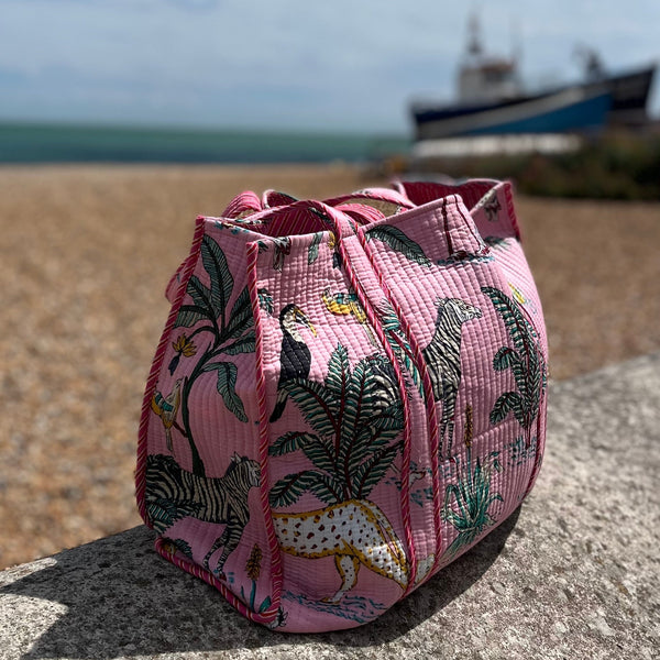 Pink fabric bag with animal print on a beach with a boat in the background