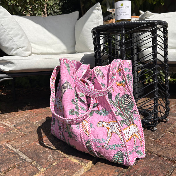 Pink tote bag with animal prints on a patio with a bottle of wine and glasses.