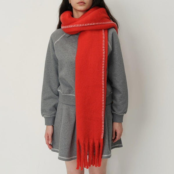 women in a grey coat with red blanket scarf and stitch detail against a white background.