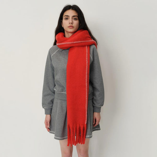 women in a grey coat with red blanket scarf and stitch detail against a white background.