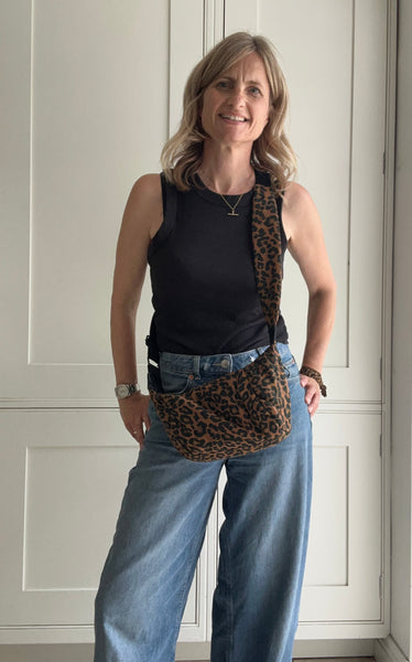 Woman wearing a black sleeveless top and blue jeans with a leopard print bag indoors.