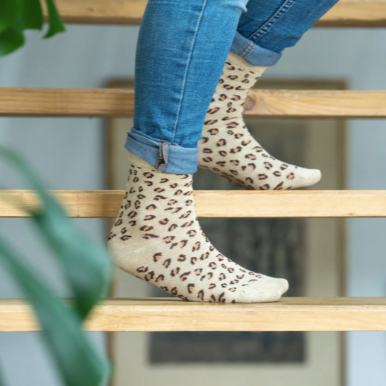 A person wearing jeans and leopard print glitter combed cotton socks with a cream heel, cuff, and toes, stepping onto a wooden staircase.