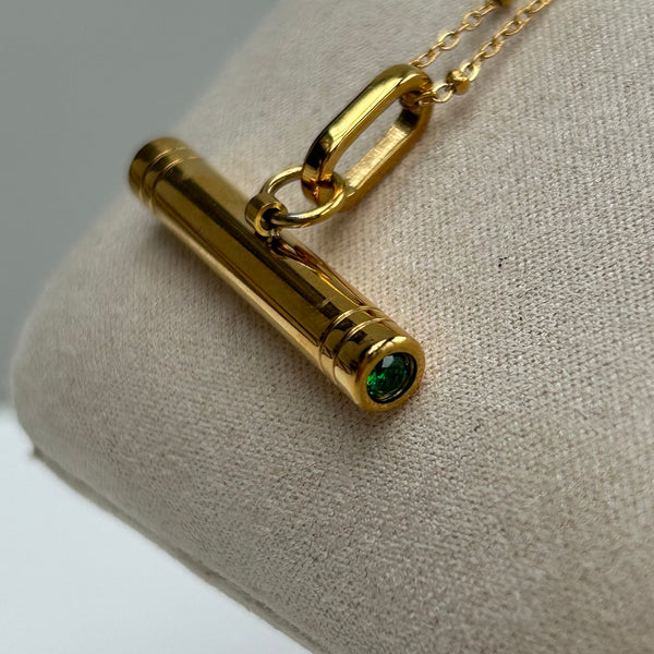 gold T-Bar pendant witth an emerald green crystal on a satellite chain on a cream linen jewellery hanger