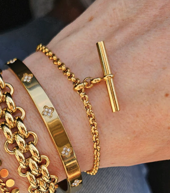 women's wrist with multiple gold bracelets including a t-bar pendant bracelet
