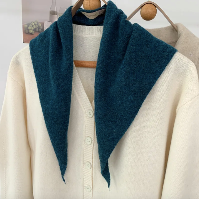 Teal blue skinny triangle scarf open over a white cardigan on a wooden hanger.