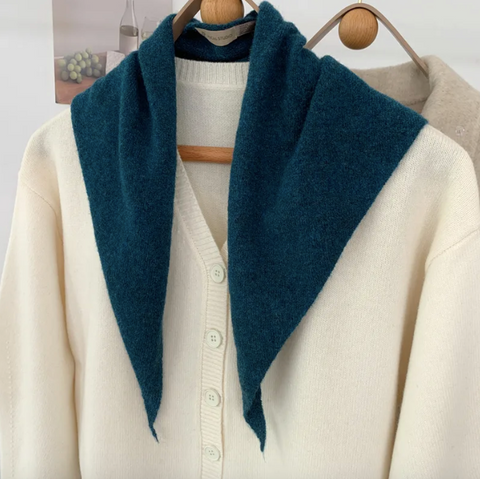Teal blue skinny triangle scarf open over a white cardigan on a wooden hanger.