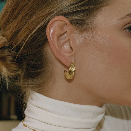 woman with a white polo neck and hair in a bun wearing textured gold hoop earrings