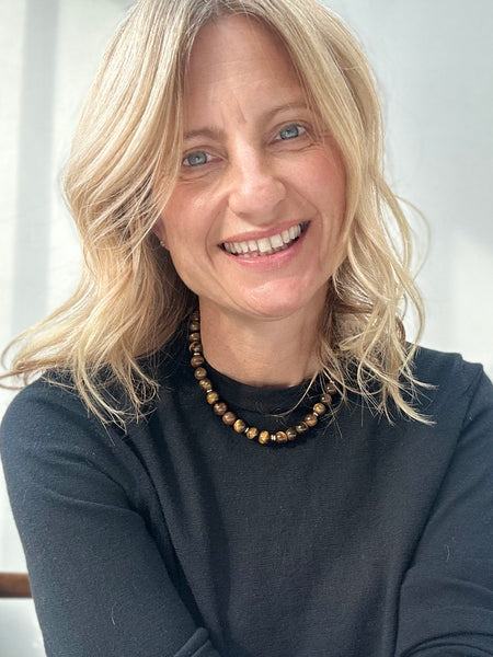 Woman with blonde hair wearing a dark top and quartz beaded necklace against a white background